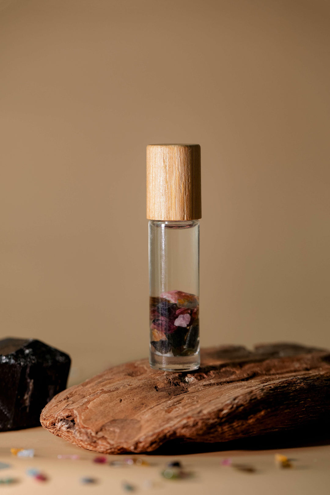A clear roller with essential oils and watermelon tourmaline crystals inside, placed on a wooden surface with a beige background.
