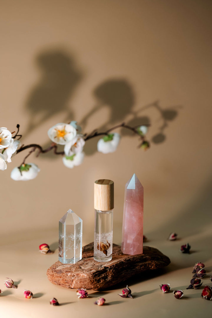 Crystal bottles and a rose quartz crystal on a wooden stand with flowers and petals on a beige background